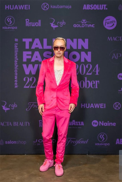 Henkilö, jolla on kirkkaan vaaleanpunainen puku, hopeanvärinen kiiltävä toppi ja vaaleanpunaiset aurinkolasit, poseeraa Tallinn Fashion Week 2024 -tapahtumassa. Heidän kiiltävä ilmeensä voisi kääntää katseita missä tahansa Kampaapo Annankadun tai Helsingin kampaapuolen tapahtumassa.
